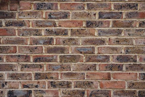 Close view of a red-brown brick wall with dark speckled bricks and pale mortar joints