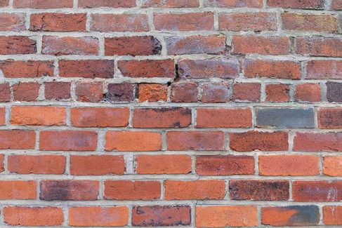 Weathered red brick wall with cracked and crumbling mortar joints